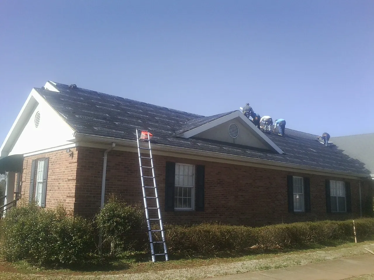Crew tearing shingles off a brick ranch roof with a ladder set — Metal Roof Repair work by our crew in Index
