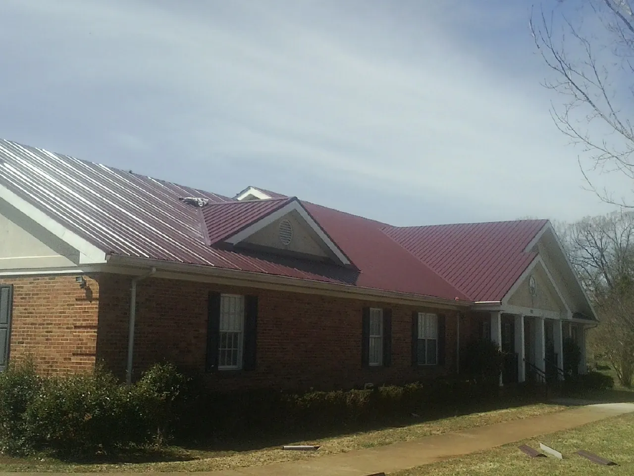 Red metal roof with gabled entries on a long brick building, from a Hail Damage Roof Repair job in Index