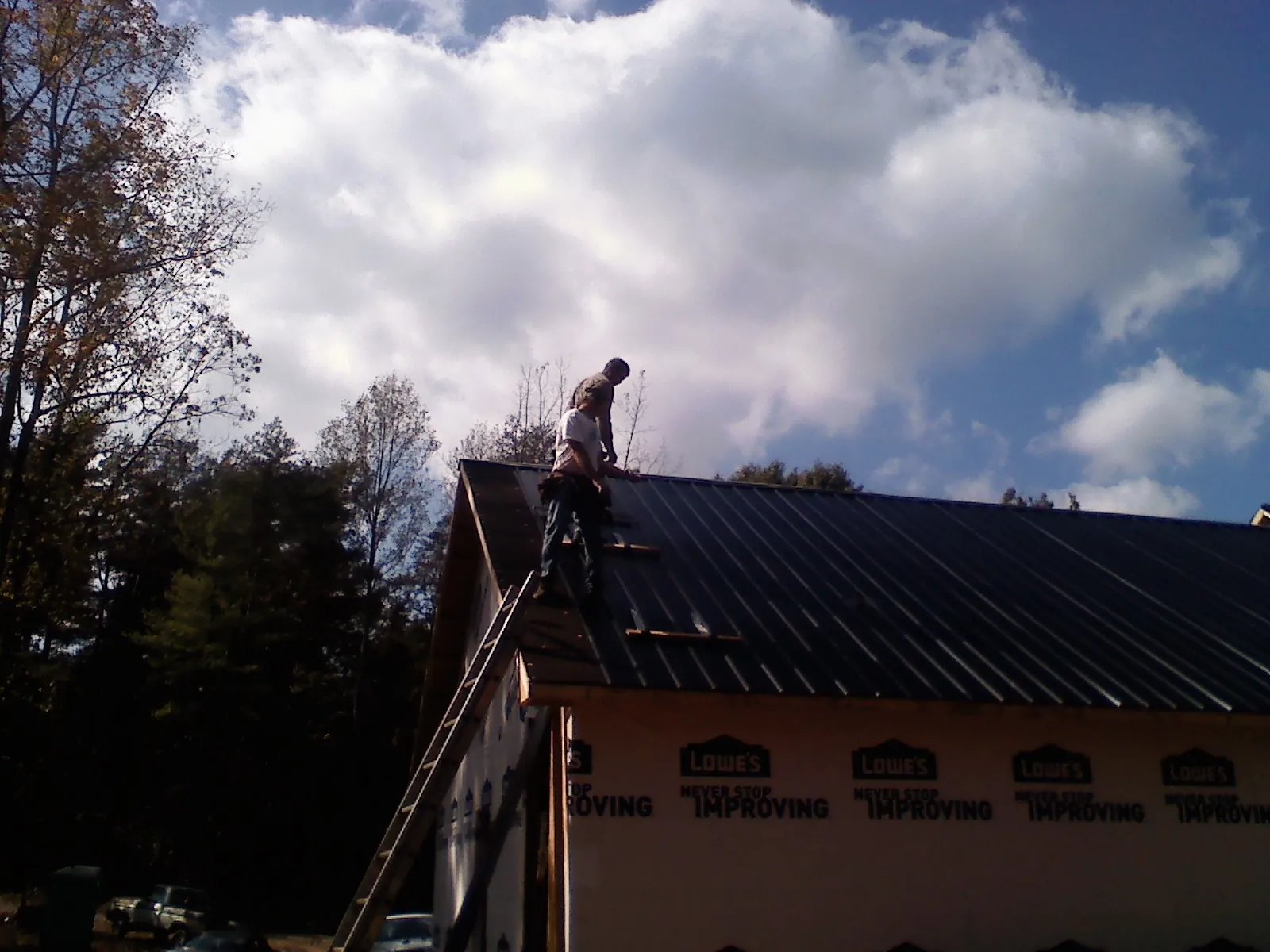 Roofer fastening dark metal panels high against a cloudy sky, from a Roof Inspection job in Index