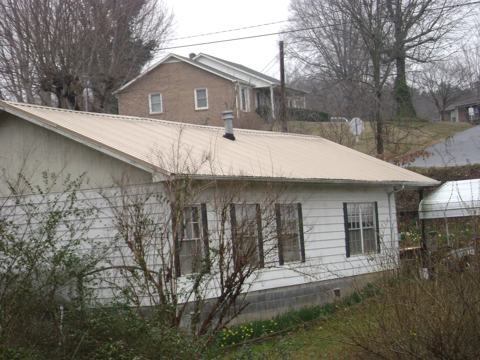 Tan metal roof on a white sided house set into a hillside — Commercial Roofing by Roofing Brothers in Index